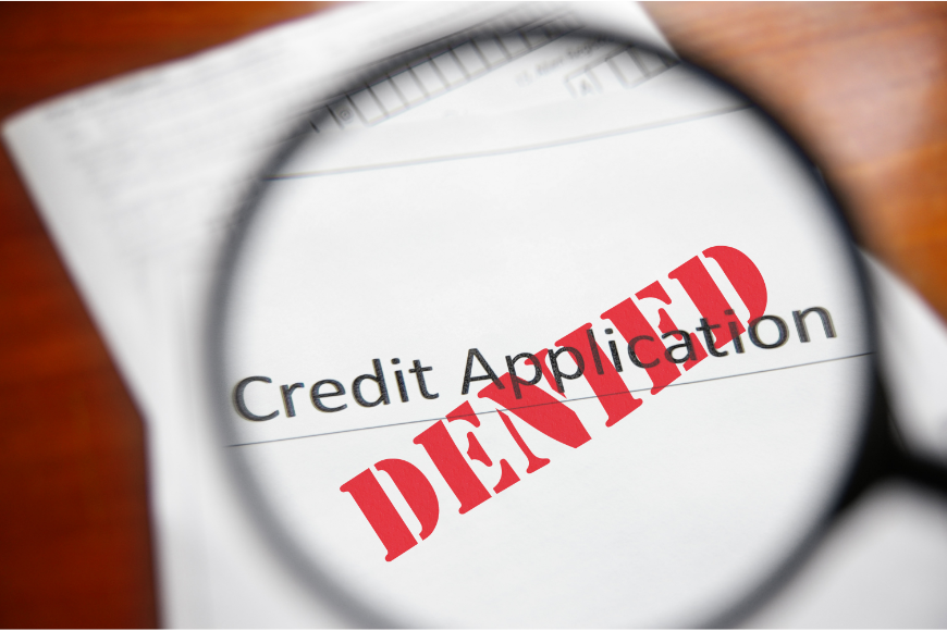 Magnifying glass over denied credit application illustrating what to do after a credit denial